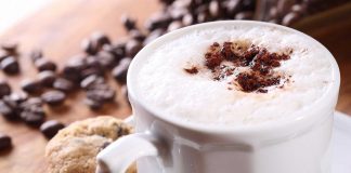 Eine Tasse Cappuccino, daneben liegen Kaffeebohnen.