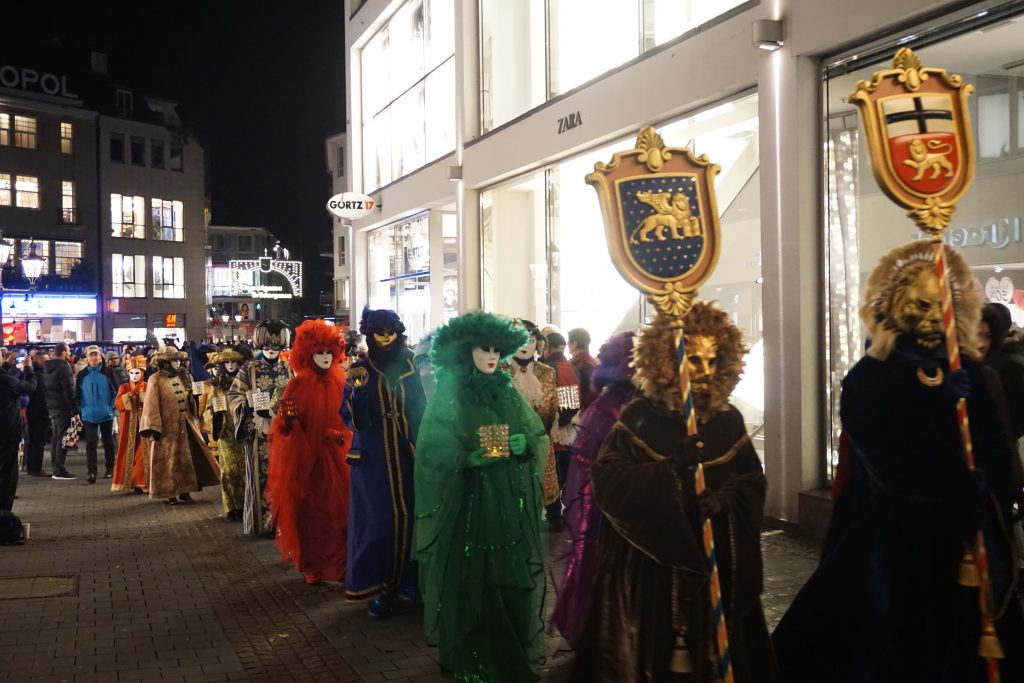 Carnevale die Venezia: hinter den Wappen der Städte Bonn und Venedig flanierten nach dem Vorbild der berühmten Karnevalskostüme Venedigs gekleidete Gestalten gemessenen Schrittes durch die City.