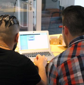 Ein Junge und ein Mann sitzen vor einem Laptop und betrachten den Bildschirm. Die Aufnahme zeigt die beiden nur von hinten.