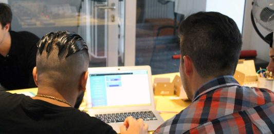 Ein Junge und ein Mann sitzen vor einem Laptop und betrachten den Bildschirm. Die Aufnahme zeigt die beiden nur von hinten.