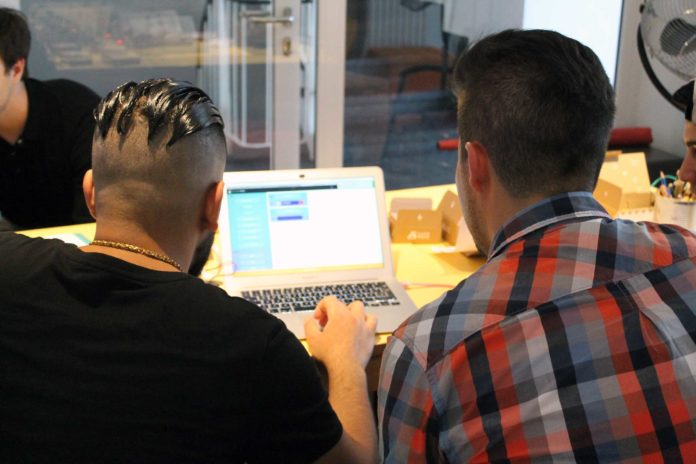 Ein Junge und ein Mann sitzen vor einem Laptop und betrachten den Bildschirm. Die Aufnahme zeigt die beiden nur von hinten.
