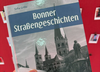 Ein Mensch hält das Buch in die Kamera, im Hintergrund eine rote Wand mit Polaroid-Fotos.