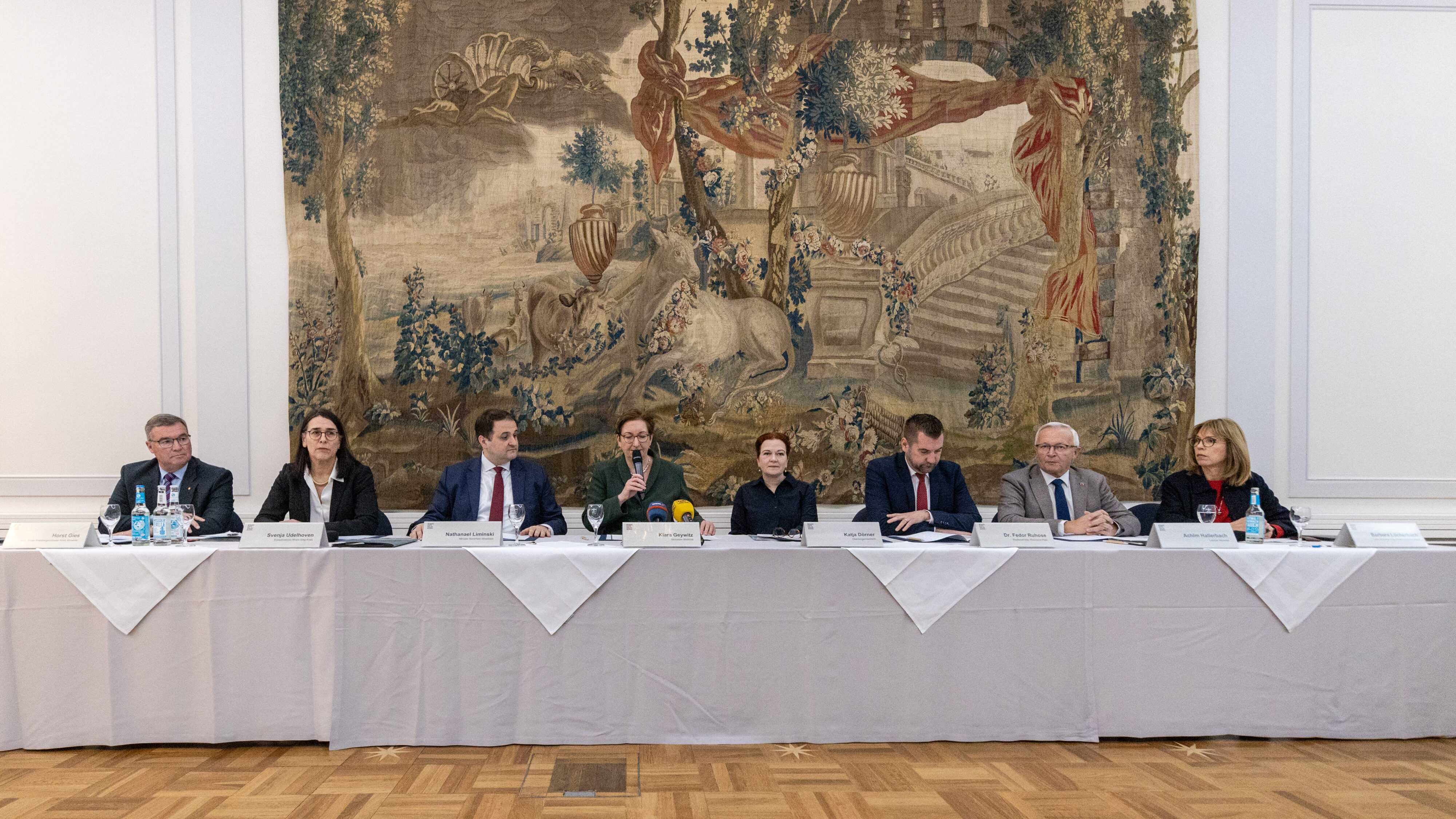 Mehrere Personen sitzen nebeneinander an einem Tisch, der mit einem weißen Tischtuch abgehängt ist. Vor ihnen stehen Namensschilder. Eine Frau in der Mitte (Klara Geywitz) spricht in ein Mikrofon.