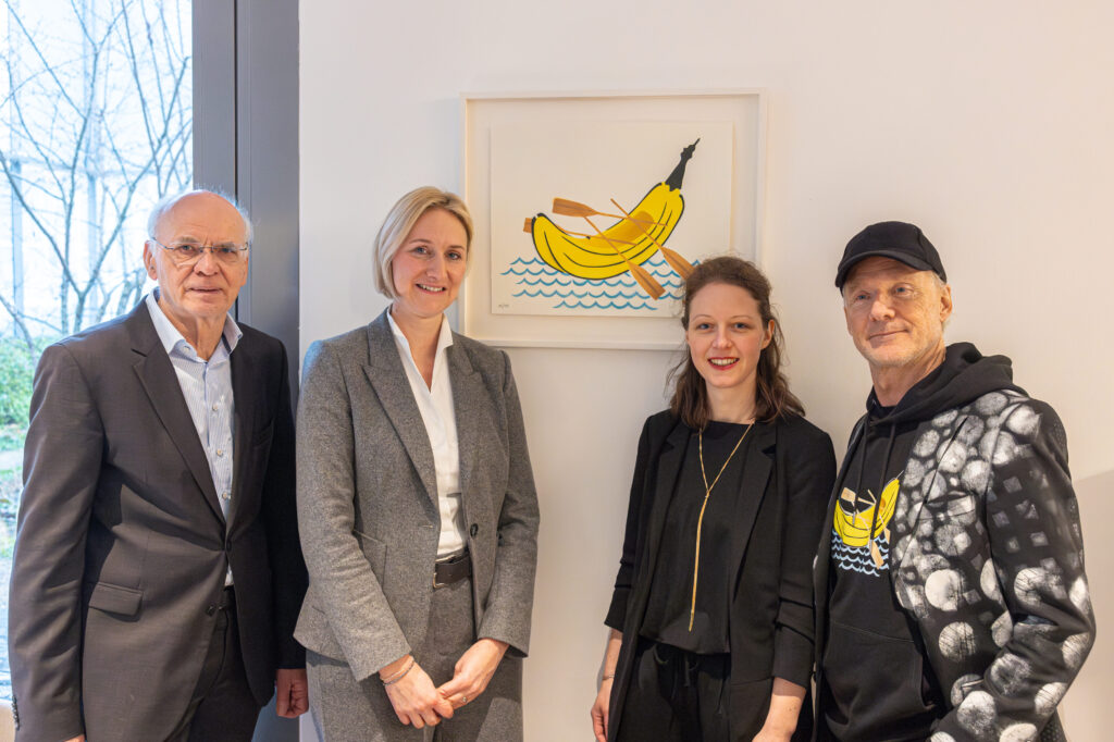 Werner PREUSKER, Galeristin Jenny GEIßLER-BENTLERS, Direktorin Dr. Frederike VOßKAMP (August Macke Haus) und Streetart Künstler Thomas BAUMGÄRTEL (Bananensprayer) stehen vor dem Bild der RUDERBANANE. Die Ruderbanane zeigt eine ausgehöhlte Banane mit Rudern an den Seiten am dem Wasser. Dargestellt ist das Kunstwerk als Graffiti im Comic Stil.